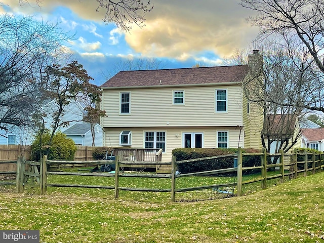 back house at dusk with a lawn and a deck