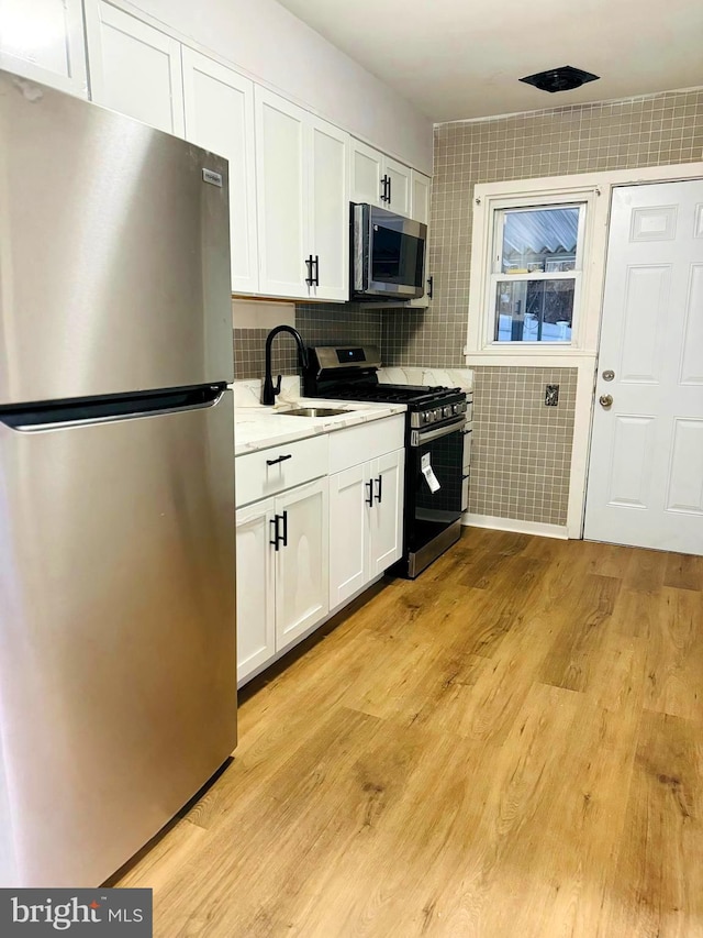 kitchen featuring white cabinets, sink, tile walls, light hardwood / wood-style floors, and stainless steel appliances