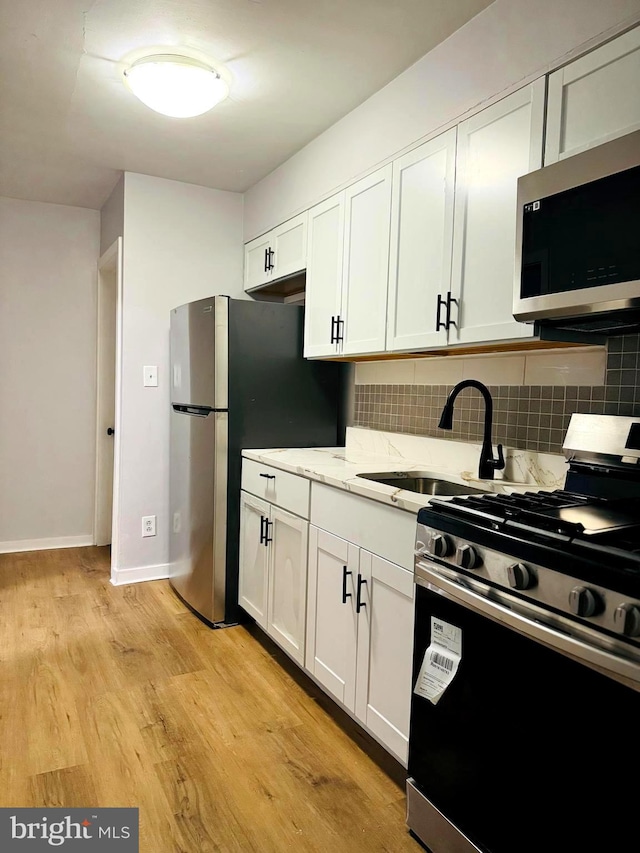 kitchen with backsplash, white cabinetry, light hardwood / wood-style floors, and appliances with stainless steel finishes