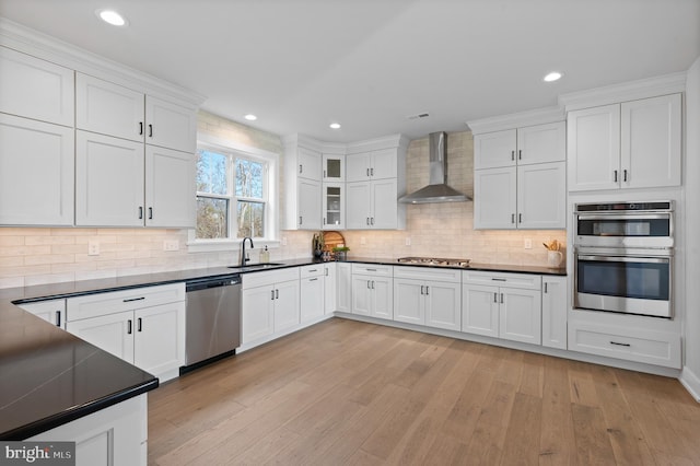 kitchen featuring stainless steel appliances, white cabinets, wall chimney range hood, dark countertops, and glass insert cabinets