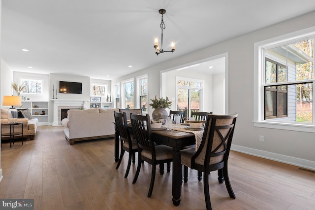 dining space featuring a fireplace, wood-type flooring, visible vents, an inviting chandelier, and baseboards