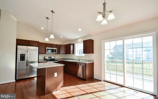 kitchen with hardwood / wood-style floors, vaulted ceiling, appliances with stainless steel finishes, decorative light fixtures, and a kitchen island