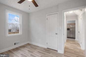 unfurnished bedroom with ceiling fan, light wood-type flooring, and stainless steel fridge with ice dispenser