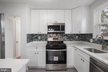 kitchen with backsplash, light stone counters, stainless steel appliances, sink, and white cabinetry