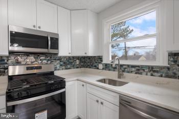 kitchen with tasteful backsplash, white cabinetry, sink, and stainless steel appliances