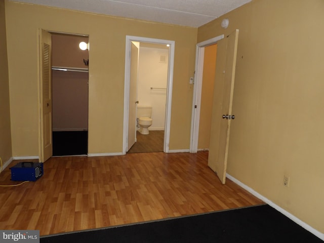 unfurnished bedroom featuring ensuite bathroom, a closet, and wood-type flooring