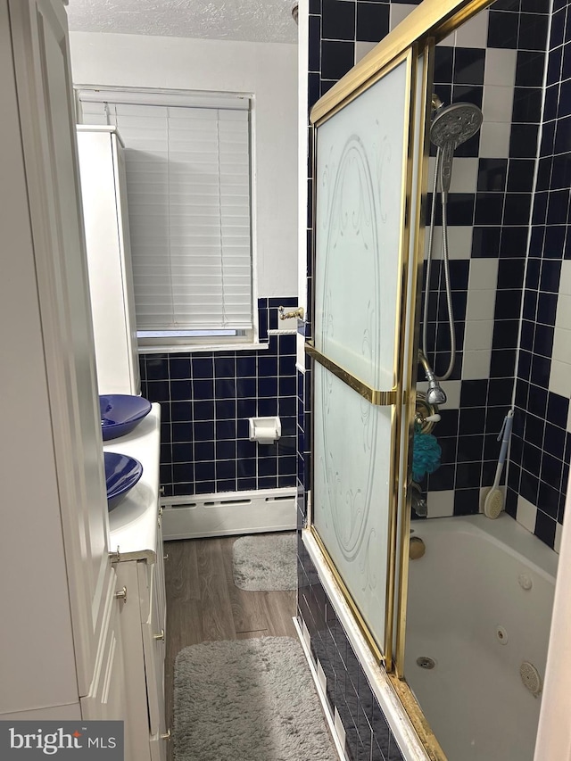 bathroom featuring hardwood / wood-style floors, combined bath / shower with glass door, tile walls, a textured ceiling, and a baseboard radiator