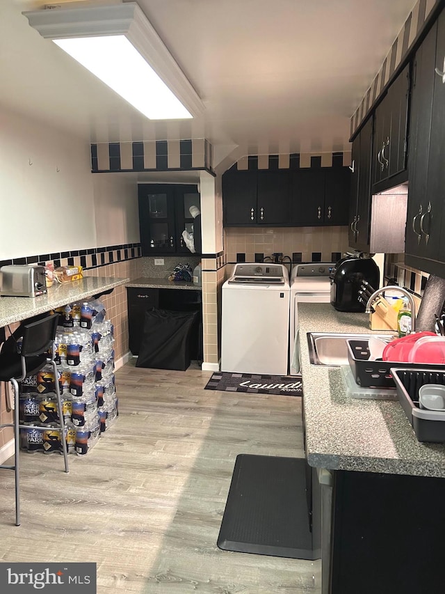 kitchen with washing machine and dryer, decorative backsplash, light hardwood / wood-style flooring, and sink