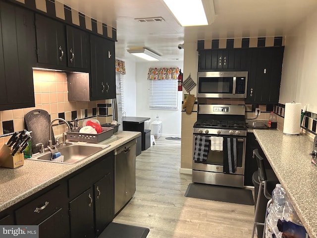 kitchen with light hardwood / wood-style floors, sink, appliances with stainless steel finishes, and tasteful backsplash