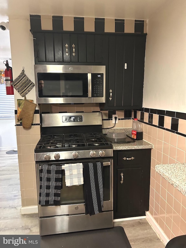 kitchen with light wood-type flooring, tile walls, and appliances with stainless steel finishes