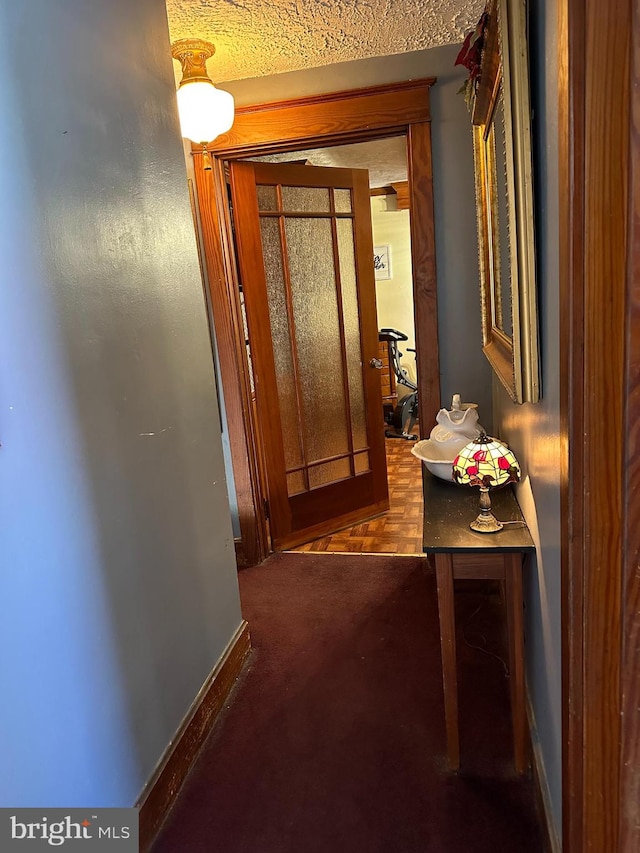 corridor with dark carpet and a textured ceiling