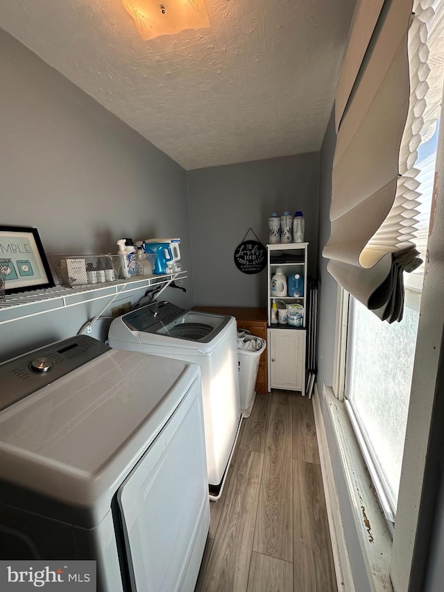 clothes washing area featuring a textured ceiling, separate washer and dryer, and light hardwood / wood-style flooring