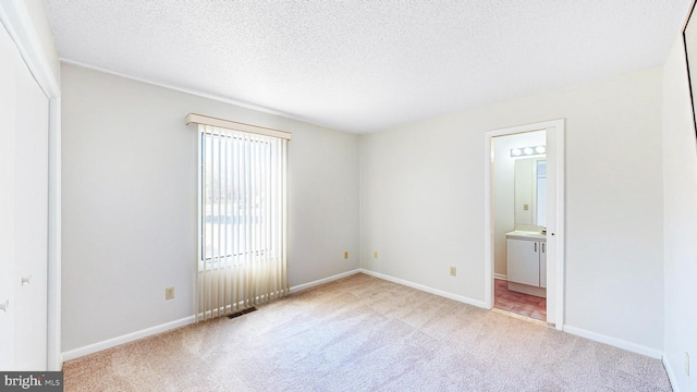 unfurnished bedroom with ensuite bath, light carpet, and a textured ceiling