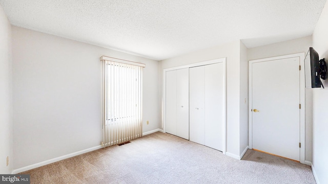 unfurnished bedroom featuring a textured ceiling, light colored carpet, and a closet