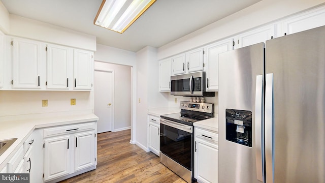 kitchen with stainless steel appliances, white cabinetry, and light hardwood / wood-style floors