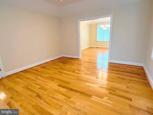 spare room featuring light wood-type flooring and an inviting chandelier