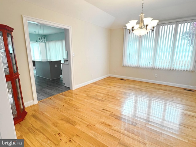 unfurnished dining area with vaulted ceiling, an inviting chandelier, and hardwood / wood-style flooring