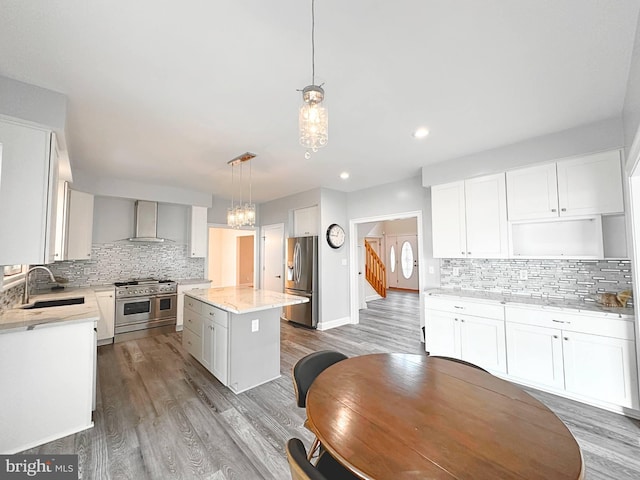 kitchen featuring appliances with stainless steel finishes, a center island, wall chimney range hood, sink, and hanging light fixtures