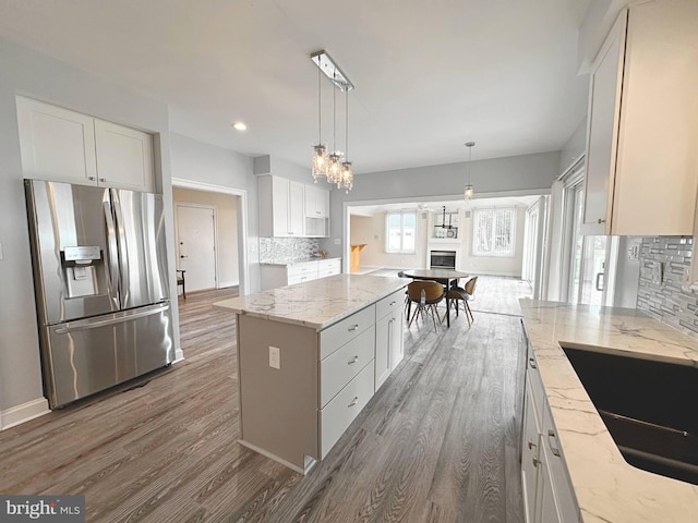 kitchen with a kitchen island, white cabinetry, backsplash, stainless steel fridge, and light stone counters