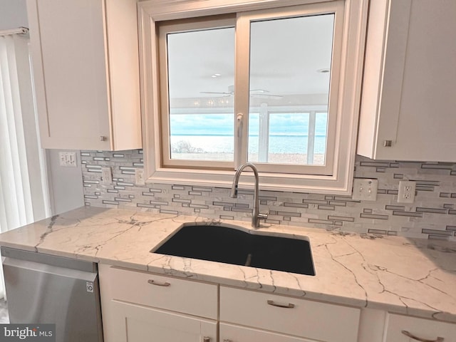 kitchen with stainless steel dishwasher, sink, a water view, white cabinets, and light stone counters