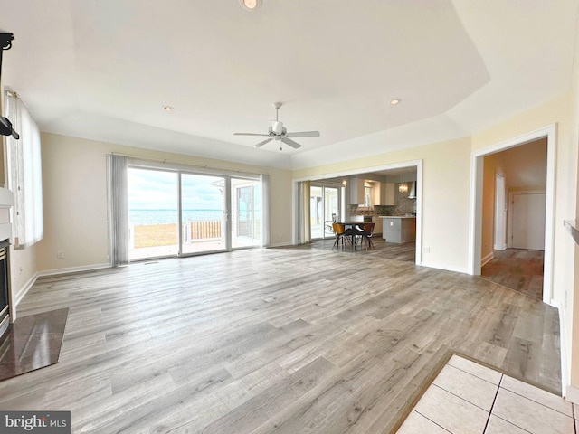 unfurnished living room with ceiling fan, a raised ceiling, and light hardwood / wood-style flooring