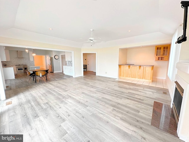 unfurnished living room with ceiling fan, a raised ceiling, and light hardwood / wood-style floors