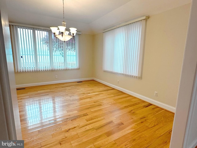 spare room with vaulted ceiling, an inviting chandelier, and light hardwood / wood-style flooring