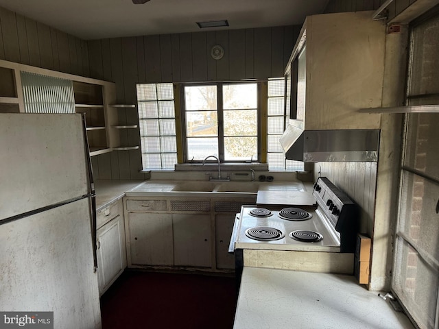 kitchen featuring wood walls, refrigerator, range with electric cooktop, and sink