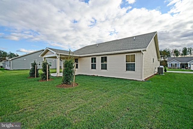 rear view of house with central AC unit and a lawn