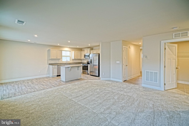 kitchen with white cabinets, light carpet, a kitchen island, and appliances with stainless steel finishes