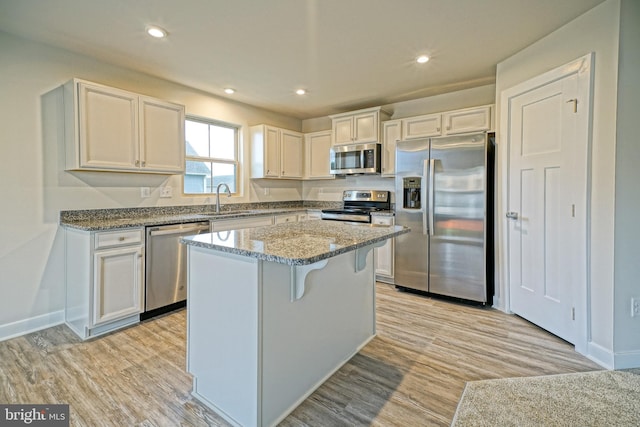 kitchen with appliances with stainless steel finishes, a center island, light hardwood / wood-style floors, and white cabinetry