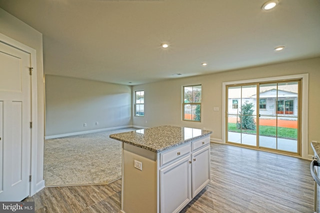 kitchen featuring white cabinets, a center island, light stone counters, and light hardwood / wood-style floors