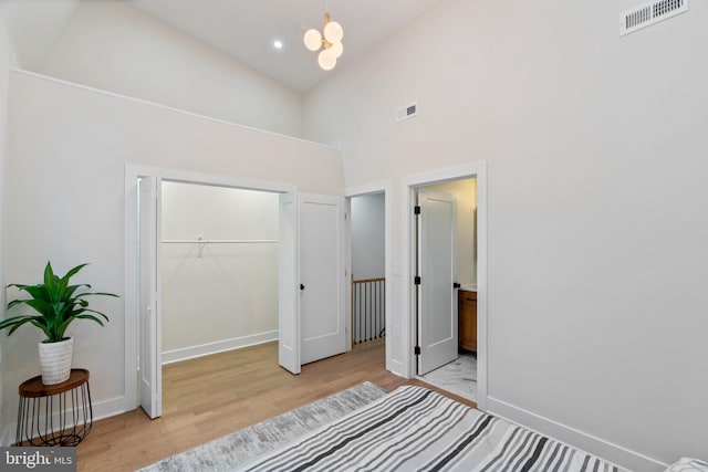 bedroom featuring light hardwood / wood-style flooring, high vaulted ceiling, a closet, and a notable chandelier