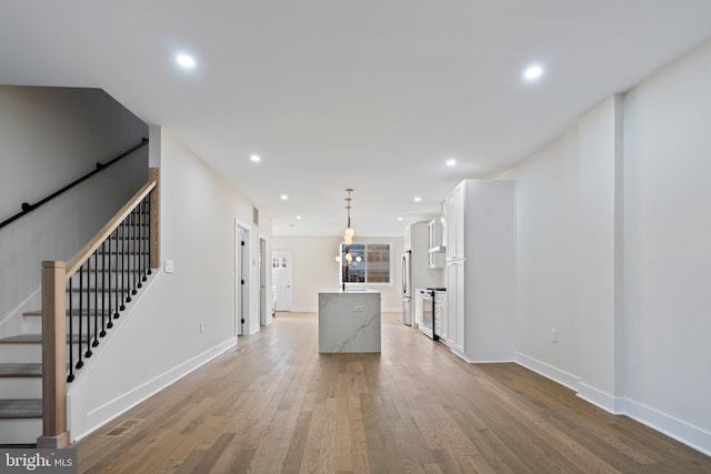 kitchen with light wood-type flooring, pendant lighting, white cabinets, a kitchen island, and stainless steel refrigerator