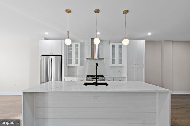 kitchen featuring wall chimney exhaust hood, tasteful backsplash, light stone counters, stainless steel fridge, and white cabinets