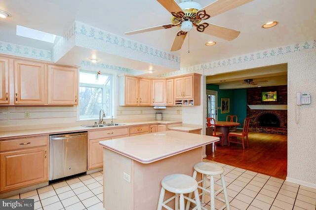 kitchen with dishwasher, sink, light tile patterned flooring, a breakfast bar area, and a kitchen island