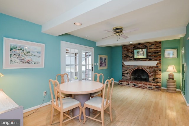 dining space featuring ceiling fan, light wood-type flooring, and a brick fireplace