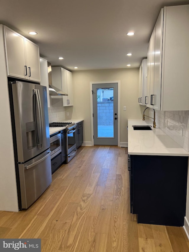 kitchen featuring wall chimney range hood, sink, light hardwood / wood-style flooring, white cabinetry, and stainless steel appliances