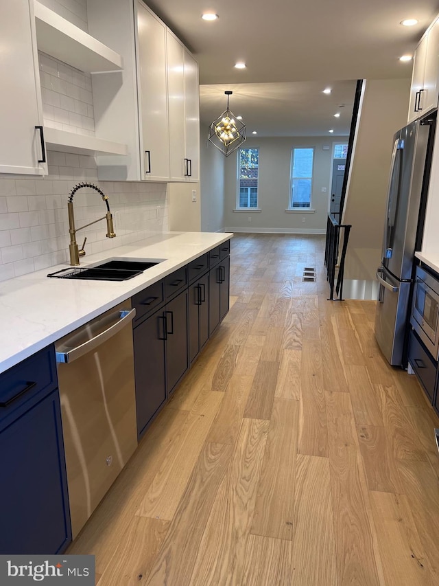 kitchen with sink, light hardwood / wood-style flooring, decorative backsplash, appliances with stainless steel finishes, and white cabinetry