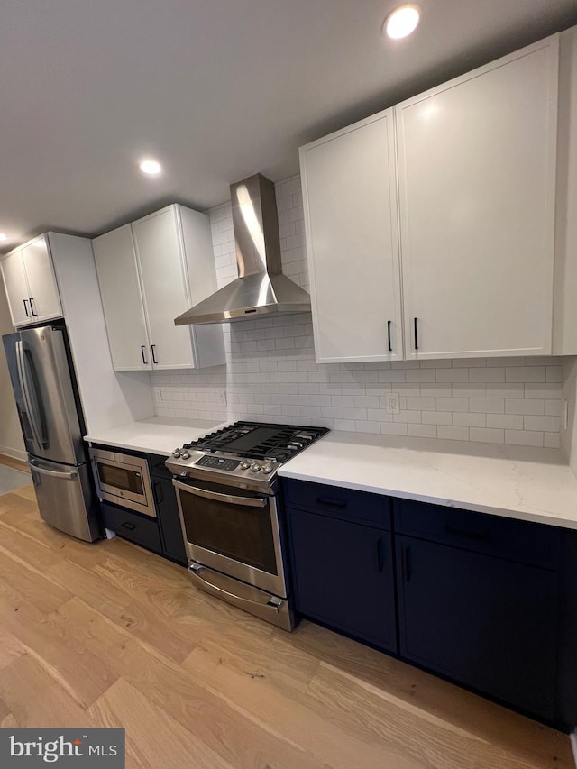 kitchen featuring white cabinetry, light wood-type flooring, wall chimney range hood, and appliances with stainless steel finishes