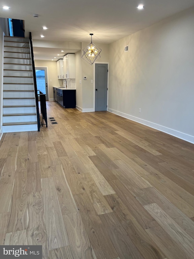 unfurnished living room featuring an inviting chandelier, sink, and light hardwood / wood-style flooring