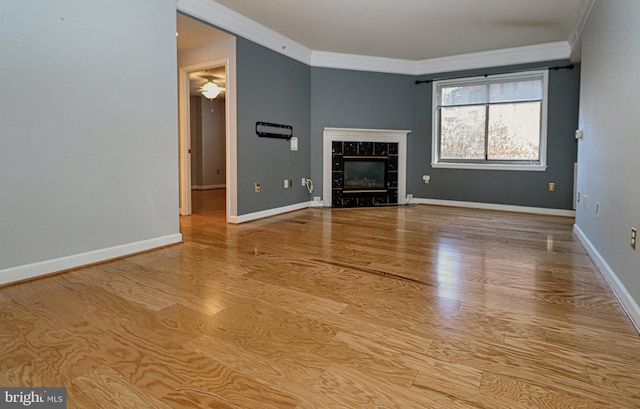 unfurnished living room featuring ceiling fan, ornamental molding, light hardwood / wood-style flooring, and a tiled fireplace