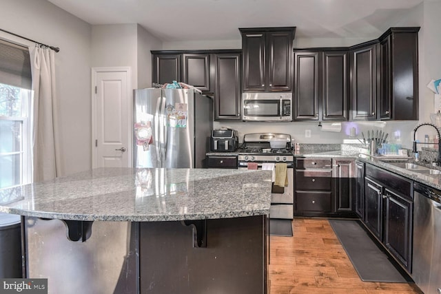 kitchen with a kitchen breakfast bar, sink, stainless steel appliances, and light hardwood / wood-style flooring