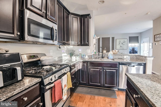 kitchen with appliances with stainless steel finishes, light wood-type flooring, light stone counters, and sink