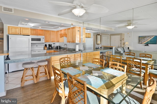 dining room featuring a tray ceiling, ceiling fan, sink, and light wood-type flooring