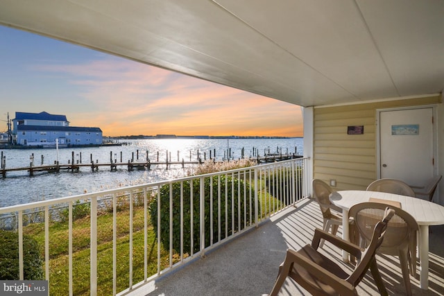 balcony at dusk featuring a water view and a boat dock