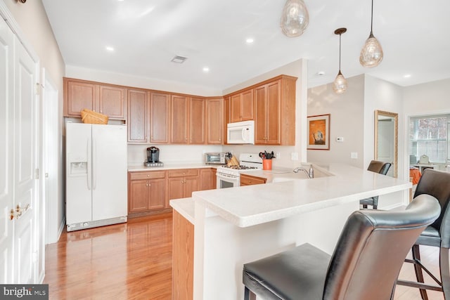 kitchen with a kitchen breakfast bar, kitchen peninsula, pendant lighting, white appliances, and light wood-type flooring