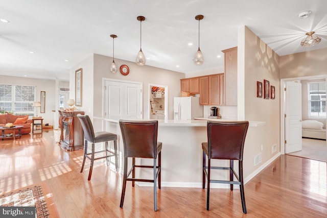 kitchen with pendant lighting, light brown cabinets, white refrigerator with ice dispenser, light wood-type flooring, and kitchen peninsula