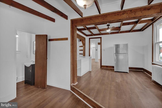 empty room featuring beamed ceiling, radiator heating unit, hardwood / wood-style flooring, and ceiling fan