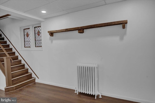 stairway with radiator heating unit, hardwood / wood-style flooring, and a drop ceiling